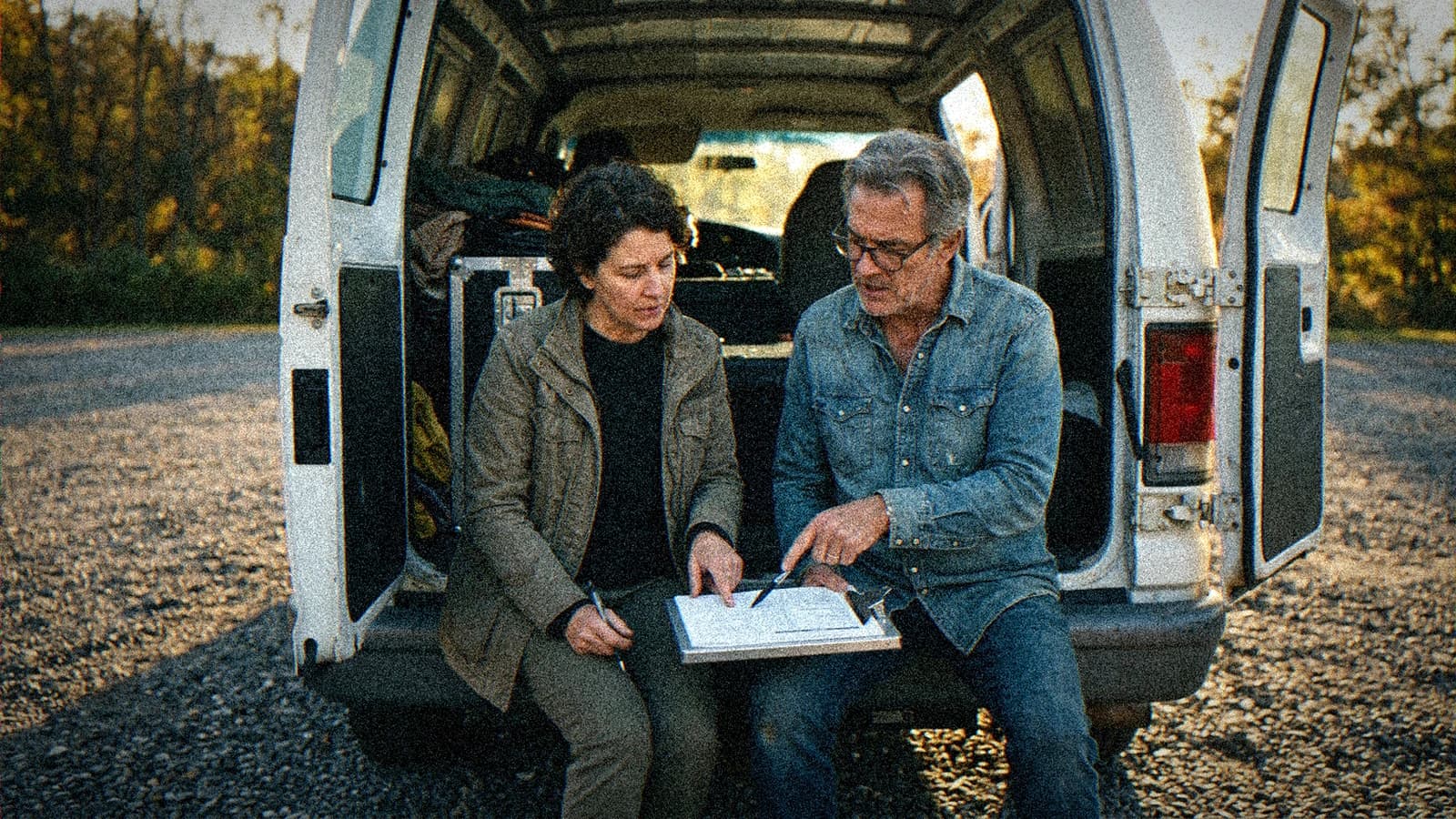 Réalisateur et productrice assis sur le hayon ouvert d'un camion de production à l'heure dorée, penchés sur une planche de plans à trier
